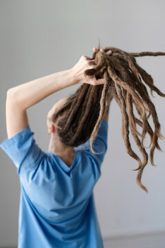 Vertical back view of Caucasian woman holding long dreadlocks out to camera minimal