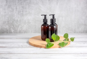cosmetic bottles on a wooden board and a sprig of mint on a gray background