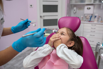 little patient covers her mouth her hands and does not allow dentist to look into her mouth.