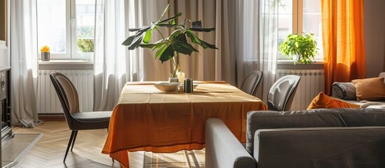 Interior of living and dining rooms featuring a grey sofa and a table draped with an orange tablecloth.