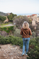 A blonde woman admires a magnificent view from the mountain of an old mansion and a picturesque valley along the coast