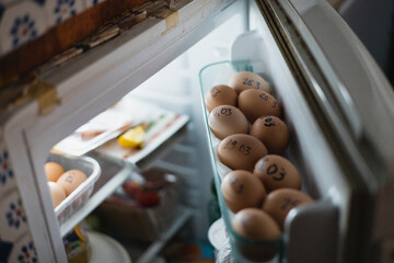 Chicken eggs from the farm on the refrigerator door - dates are written on the shell with a marker and sorted by freshness