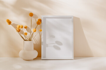 Mockup empty photo frame with vase, dry flower bouquet and beautiful sunlight shadows. Wooden photo...