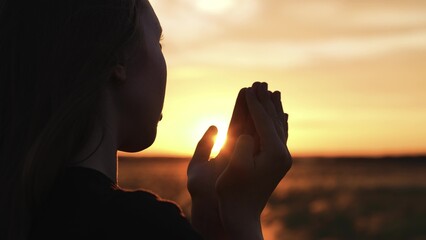 Woman praying with folded hands at sunset silhouette. Religious pious orthodox christian spiritual believing faithful girl at morning dawn sunrise reading prayer bible turning to god jesus christ. - obrazy, fototapety, plakaty