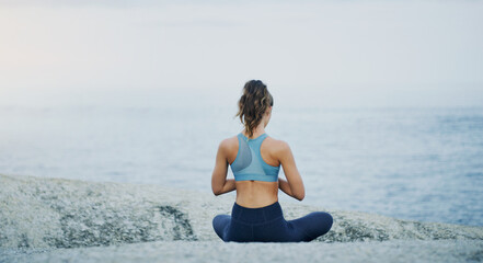 Prayer, yoga or woman in beach meditation for peace, wellness or mindfulness in outdoor nature. Chakra, calm or back view of girl on rock at sea or ocean for awareness or balance in pilates to relax