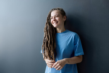 Minimal waist up portrait of young Caucasian woman with long dreadlocks standing by grey wall and...