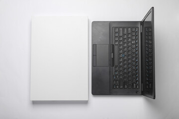 New black modern laptop with white cardboard box on white background. Top view. Flat lay