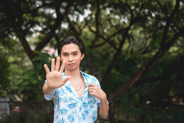 Young man in a blue tropical shirt posing in a lush green forest