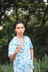 Young man in a blue tropical shirt poses in a lush forest setting