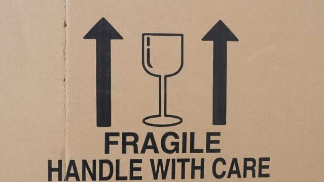 A close-up of a cardboard box. Reading fragile, handle with care sign and upright container arrows. Concept for moving home, packaging, removals, relocating and storage transportation. Static shot 4K.