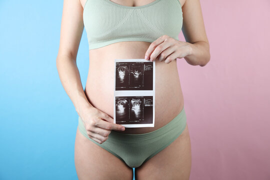 Pregnant woman in underwear shows ultrasound scan image in blue pink background