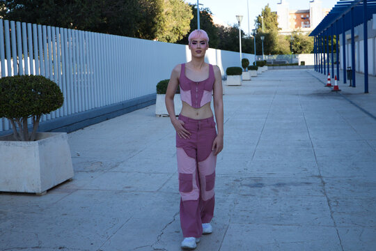 Young gay guy with pink hair and makeup walks down the street and poses for the photo. The boy is dressed in pink with modern clothes. Concept of equality and LGBTQ rights.
