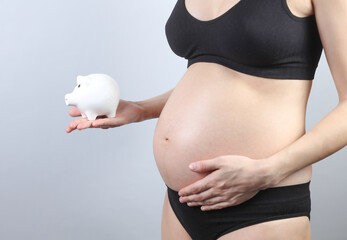 Pregnant woman in underwear holding piggy bank on gray background. Maternal capital