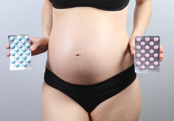 Pregnant woman in underwear holding pills blisters on gray background