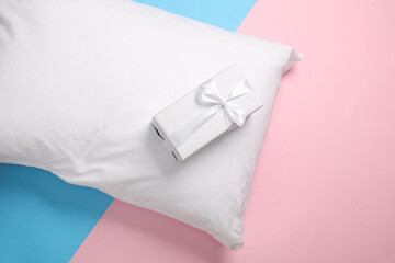 White pillow with gift box on a blue-pink pastel background. Top view