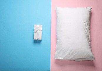 White pillow with gift box on a blue-pink pastel background. Top view