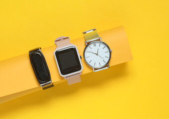 Modern smart and analog watches and bracelet on a yellow background.