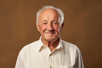 Portrait of a grinning man in his 80s wearing a simple cotton shirt in soft brown background