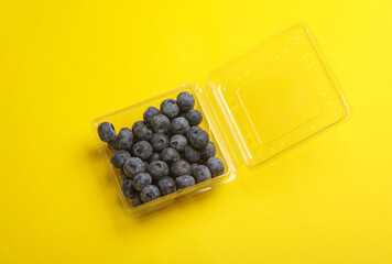Blueberries in a transparent plastic box on a yellow background. Top view