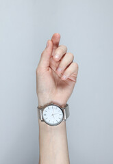 Female hand with analog wristwatch on gray studio background
