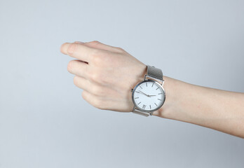 Female hand with analog wristwatch on gray studio background