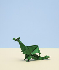 Green Origami dragon with eyes on pastel background. Creative layout