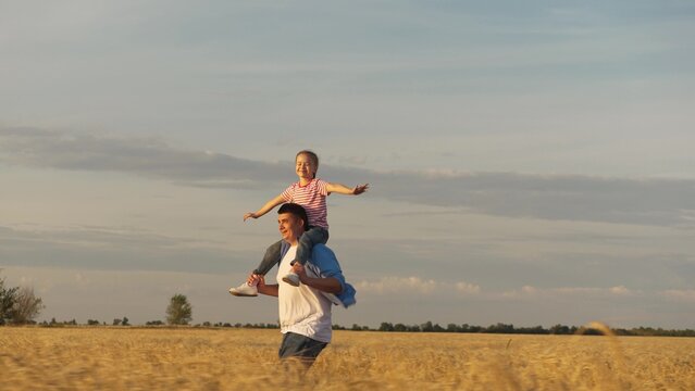 Smiling family father and daughter running flying at sunset dry wheat field with positive emotion. Happy male parent and little girl kid flight plane imagination together overjoyed freedom outdoor