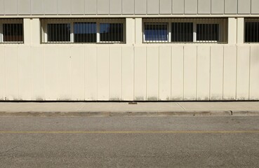 White and gray prefab concrete wall with a row of barred windows. Cement sidewalk and street in front. Background for copy space.