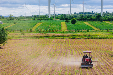 eco power green farming concept. Farmer drives a fertilizer spray plant row agriculture field at wind turbine power generator farm background