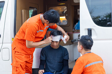 A man with a bandaged head is being helped by two other men in orange. The scene is serious and focused on the injured man
