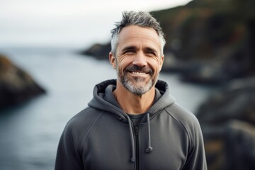 Portrait of a smiling man in his 50s dressed in a comfy fleece pullover on rocky shoreline background