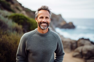 Portrait of a smiling man in his 50s dressed in a comfy fleece pullover isolated on rocky shoreline background