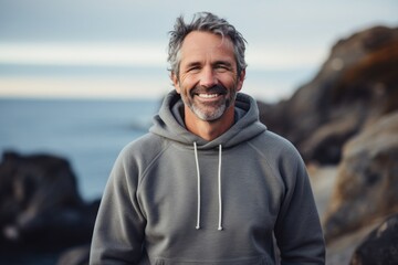 Portrait of a smiling man in his 50s dressed in a comfy fleece pullover in rocky shoreline background