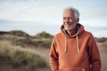 Portrait of a happy man in his 70s dressed in a comfy fleece pullover while standing against serene dune landscape background