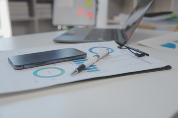 Close up view of simple workspace with laptop, notebooks, coffee cup and tree pot on white table with blurred office room background