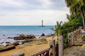 View of a lighthouse in the sea near a rocky shore with palm trees. End of the World Park, Sanya.