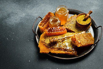 Honey background. Assortment of honey, honeycombs, pollen on a metal tray. On a black stone...