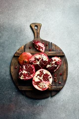  A wooden kitchen cutting board with a piece of fresh pomegranate. On a concrete background. © Yaruniv-Studio
