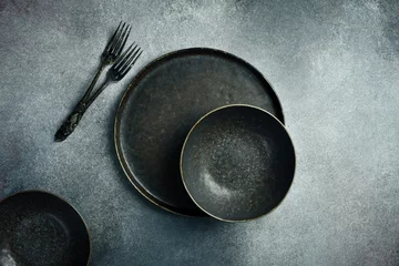  An aesthetic arrangement of vintage dark bowls, plates and cutlery on a gray concrete background. Free space for text. © Yaruniv-Studio