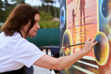 Female painter draws picture with paintbrush on canvas for outdoor street exhibition, close up side...
