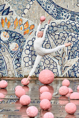 Young hairless girl ballerina with alopecia in white futuristic suit dancing outdoor and jumps with pink sphere on abstract mosaic Soviet background, symbolizes self expression