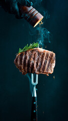 Beef steak on a fork with a pepper mill, frozen pepper particles in the photo. Grilled steak. On a black background.