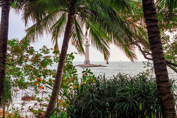 View of the lighthouse in the sea near the rocky shore through the palm trees. Sanya, China