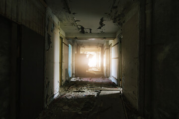 Fototapeta na wymiar Decayed corridor in derelict building with sunlight streaming through the end.