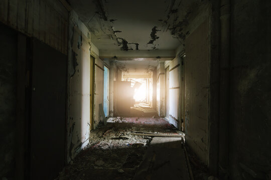 Decayed corridor in derelict building with sunlight streaming through the end.