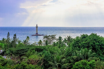 View of a lighthouse in the sea near a rocky shore with palm trees. End of the World Park, Sanya.