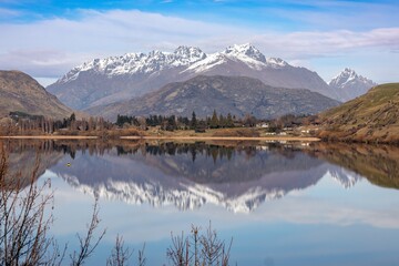 Aerial: Mirrored Lake Hayes and mountains with snow, Queenstown, Otago, New Zealand.
