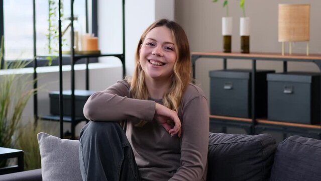 Portrait of a young Caucasian laughing woman resting while sitting on sofa, at home living room. content lady individuality and femininity concept.