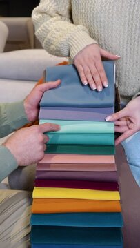 A man and woman choosing upholstery fabric color and texture from various colorful samples for sofa in a store. Vertical video