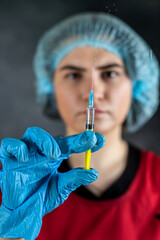 Woman doctor in red uniform, blue latex gloves hold syringe with vaccine